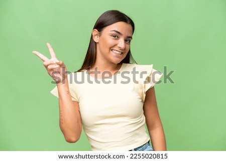 Young caucasian woman isolated on green chroma background smiling and showing victory sign
