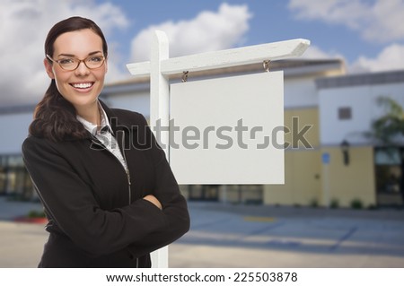Attractive Serious Mixed Race Woman In Front of Vacant Retail Building and Blank Real Estate Sign.