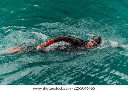 A triathlete in a professional swimming suit trains on the river while preparing for Olympic swimming Royalty-Free Stock Photo #2255046465