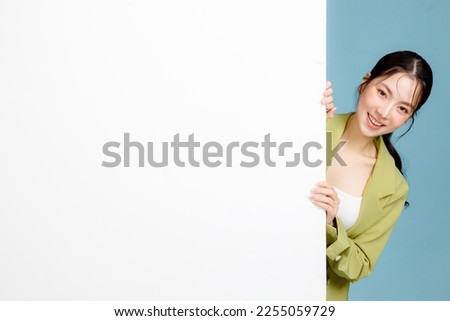 Young happy smiling successful employee business woman 20s in casual green jacket peeking out blank whiteboard isolated on pastel blue background. Female entrepreneurs, office worker concept. Royalty-Free Stock Photo #2255059729