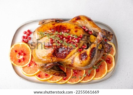 Chicken baked whole to appetizing crispy crust with pomegranate and red orange. Traditional New Year and Christmas dish. Close-up, selective focus, white background.