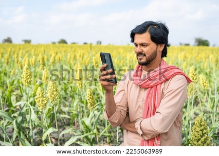 Farmer busy using mobile phone at agricultural farm land showing with copy space - concept of technology, connection and modern village farmer
