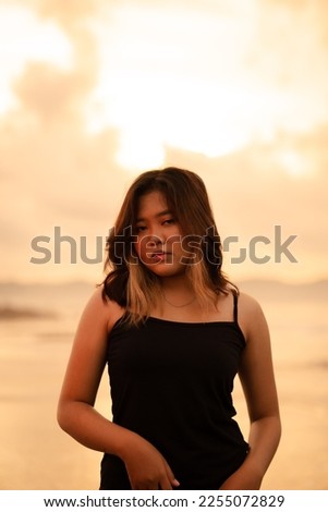 An Asian woman poses with a dirty and angry expression when wearing a black dress on the beach in the morning