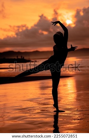 A Balinese woman in the form of a silhouette performs ballet movements very deftly and flexibly on the beach with the waves crashing in the afternoon