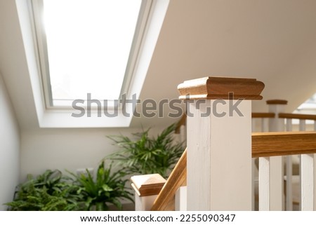 Shallow focus of a wooden bannister at the top of a recently converted loft space. Half way down the stairs are house plants on a ledge and nearby skylight window. Royalty-Free Stock Photo #2255090347