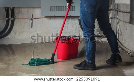 Woman mopping flood from water leaks in basement or electrical room. Water damage from rain, snowmelt or pipe burst coming from multiple cracks and leaks in concrete wall and ceiling. Selective focus. Royalty-Free Stock Photo #2255091091
