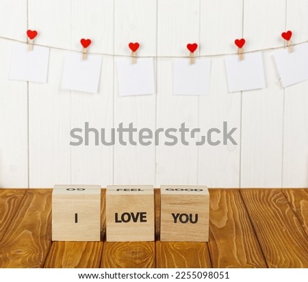 white pieces of paper on clothespins with a heart on a wooden background, a wooden inscription I love you close-up