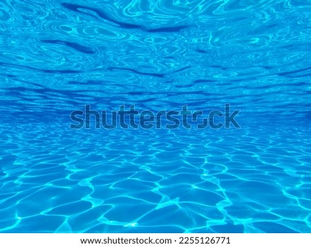 The view through a viewing port between floor, bottom and surface of luxury swimming pool and blue water with sun reflections at the resort  Royalty-Free Stock Photo #2255126771