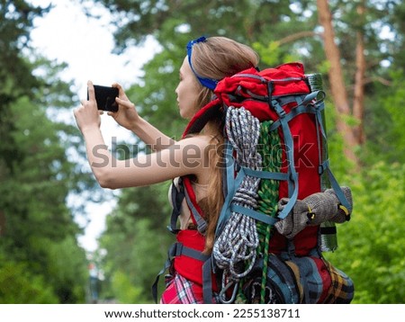 Woman taking a photo with smartphone while walking in the forest. She sends photos to her friends.