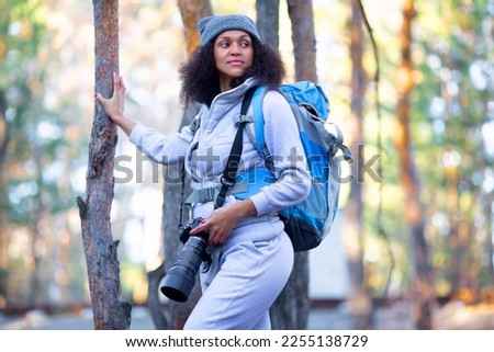 Photo of an African American woman in the forest with a camera. She watches and photographs birds.