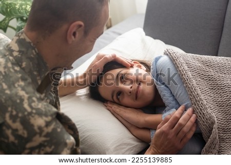 Affectionate military father kissing his daughter who is sleeping on the sofa at home