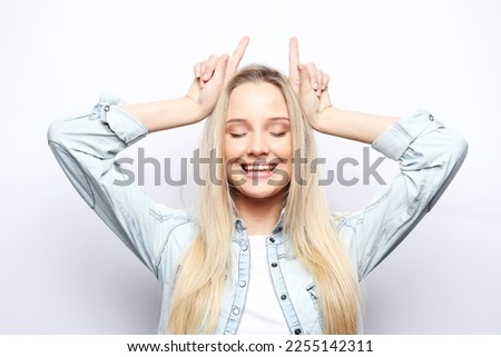 Lifestyle, emotion and body language concept: Young blonde woman wearing casual doing funny gesture with finger over head as bull horns