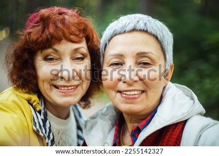 Multiracial smiling elderly women having fun during trekking day in to the wood - make selfie with smartphone.