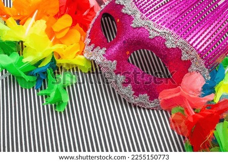 pink carnival mask on a black and white striped background and colorful  flowers