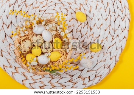 Easter candy chocolate eggs and almond sweets lying in a bird's nest decorated with flowers and feathers on white background. Happy Easter concept.