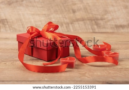 Happy Valentine's Day, Mother's Day and birthday greeting card. Red gift box with a red satin ribbon bow with red candles in the shape of hearts on a wooden background.
