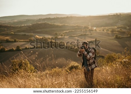 Cheerful man with a digital camera enjoying himself while spending an autumn day on the hill. Copy space. Royalty-Free Stock Photo #2255156149