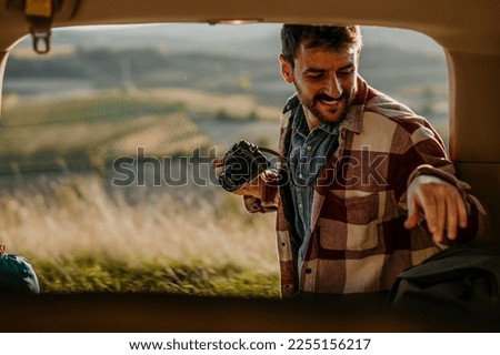 A smiling man sitting in his car truck, holding a digital camera and about to photograph wildlife.