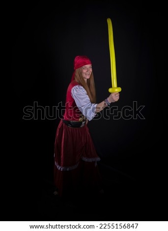 woman with long hair dressed as a pirate in a red suit and with a yellow balloon in the shape of a sword in her hand and on a black background photography of party events