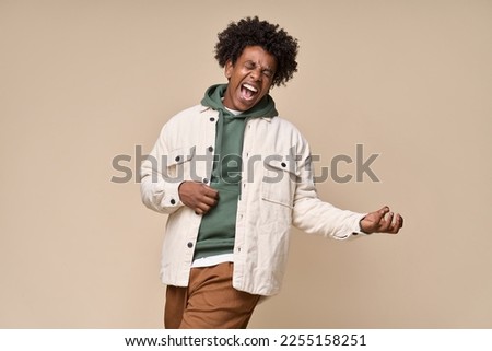 Crazy cool hipster African American guy pretending playing guitar having fun isolated on beige background. Funny funky ethnic generation z teenager fashion model screaming singing and dancing. Royalty-Free Stock Photo #2255158251