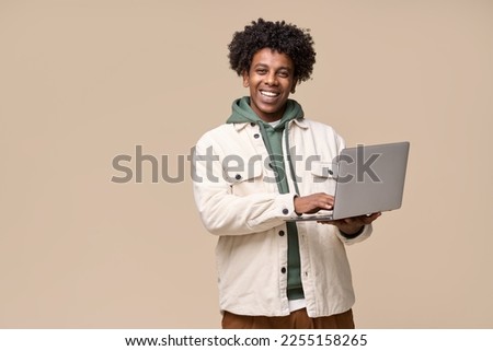 Young happy cool African American teenager student boy holding laptop using computer technology advertising elearning remote education and online webinars isolated on light beige background.