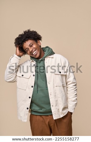 Happy young African American gen z guy isolated on beige background. Smiling hipster ethnic teen student, cool curly ethnic generation z teenager fashion model standing laughing, vertical shot.