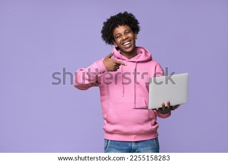 Happy African American teenager student boy holding device pointing at laptop computer technology advertising remote learning, online webinars, training courses isolated on light purple background. Royalty-Free Stock Photo #2255158283
