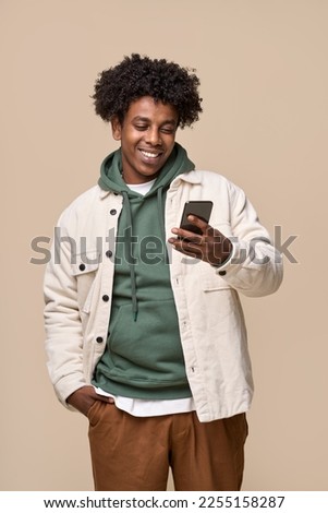 Smiling cool ethnic guy holding smartphone isolated on beige background. Happy African American teen using mobile cell phone advertising shopping or social network apps commercial promotion. Vertical