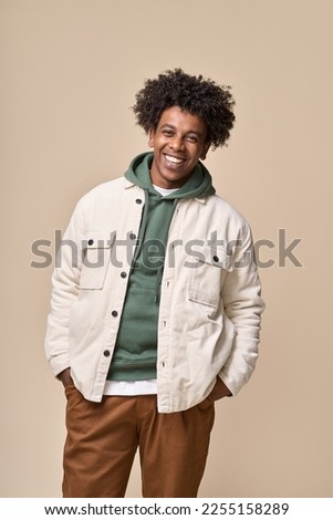 Happy young African American gen z guy isolated on beige background. Smiling hipster ethnic teen student, cool curly ethnic teenager stylish fashion model standing laughing, vertical shot.