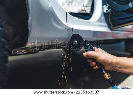Close-up of male hand holding small rotary saw tool cutting out fragment of body of car. Garage work. Horizontal indoor shot. High quality photo