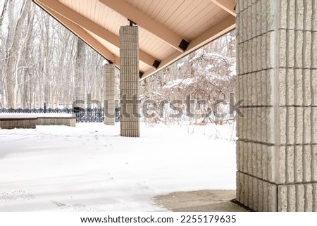 Snow covered porch surrounded by bare trees with cast iron fence in background.