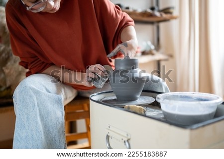 Attentive woman sits in pottery workshop and diligently does what she loves, which brings income and pleasure. Female makes aesthetic items for home with own hands. Working with clay for mental health