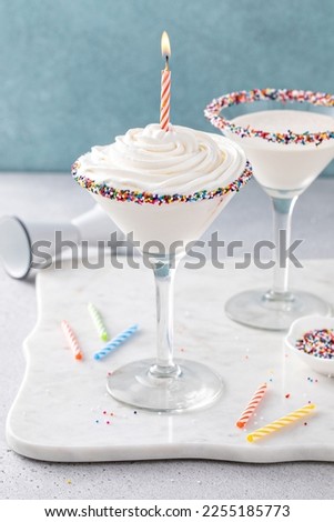 Birthday cake martini with sprinkles on the glass rim topped with whipped cream with birthday candle