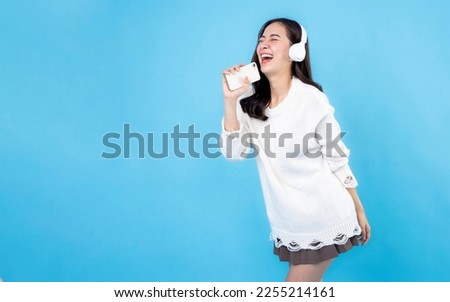 Happy young woman in headphones listening to music on light blue background. Smiling caucasian young woman listening to the podcast e-book music song singer rock band in headphones earphones. Royalty-Free Stock Photo #2255214161