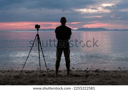 Photographer with camera on tripod on the beach at sunset. Klong Muang Beach, Krabi Province, Thailand.