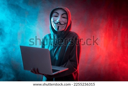 Hacker with anonymous mask with a computer and with a background of smoke and colored led Royalty-Free Stock Photo #2255236315