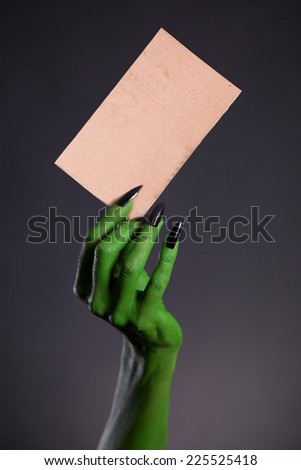 Green monster hand holding blank piece of cardboard, horror Halloween theme  