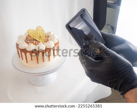 chef pastry baker making a reel of a salty caramel frosted dripping cakes with meringues and chocolate heart topper with smarphone photo