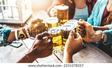 Happy friends cheering beer glasses at brewery pub restaurant - Group of young people enjoying happy hour celebrating party outdoors - Beverage life style concept with guys and girls hanging out 