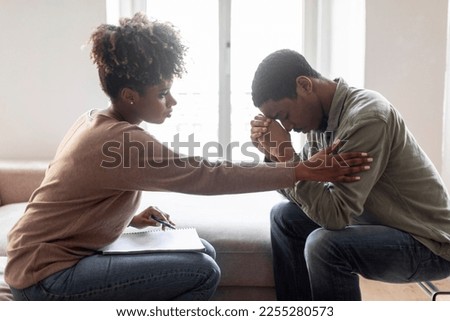 Black woman in casual outfit psychologist comforting touching shoulder upset frustrated young man patient, unhappy african american guy have therapy session, suffering from depression, side view shot Royalty-Free Stock Photo #2255280573