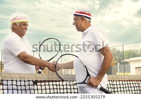Active senior tennis players meeting at the net after a match and talking.