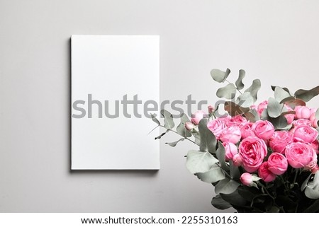 Blank canvas mockup hanging on grey wall and pink flowers in interior. Empty white canvas and floral decor