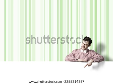 Young funny guy in checked shirt pointing with finger at blank banner