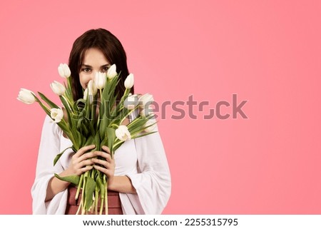 Glad young caucasian female in casual enjoy aroma bouquet of flowers, birthday and free time isolated on pink background, studio. Celebration holiday at spring, sale, fashion, lifestyle, ad and offer Royalty-Free Stock Photo #2255315795