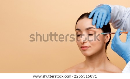 Cosmetologist Doctor Making Botox Injection For Eyes Area To Young Indian Woman, Attractive Hindu Lady Getting Anti-Wrinke Treatment While Standing Over Beige Studio Background, Copy Space Royalty-Free Stock Photo #2255315891