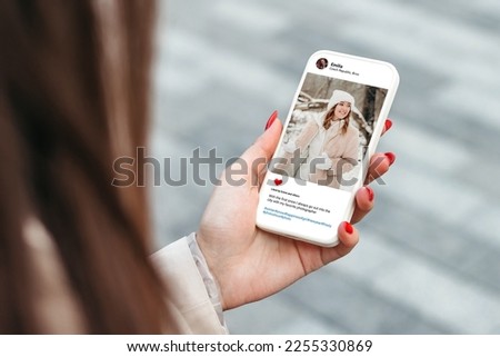 Woman looking at beautiful model's photo on mobile phone screen walking in winter forest