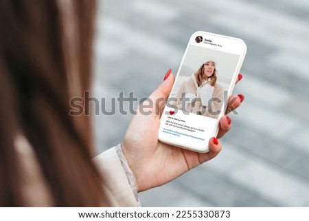Woman looking at beautiful model's winter photo on mobile phone screen in social networks