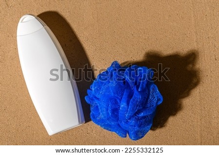 White container with shampoo for hair care. Blue washcloth on the sand.