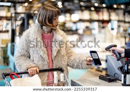 Woman pays with a QR code or scans her loyalty card on phone at a supermarket checkout. Concept of modern retailing technologies in supermarket Royalty-Free Stock Photo #2255339317