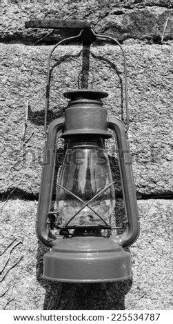 The old kerosene lantern hanging on the stone wall of  antique farmhouse. France. Aged photo. Black and white.